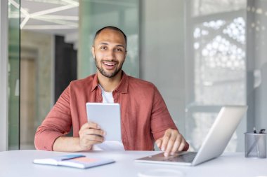 İş yerindeki genç ve başarılı bir işadamının portresi, elinde tablet bilgisayarla kameraya bakan bir adam, iş yerinde dizüstü bilgisayar kullanan bir ofis çalışanı..