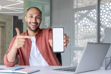 İş yerindeki adam kameraya beyaz telefon ekranı gösteriyor, iş adamı çevrimiçi finans hizmetleri uygulaması tavsiye ediyor ve reklamını yapıyor, yeni program bankalıyor.
