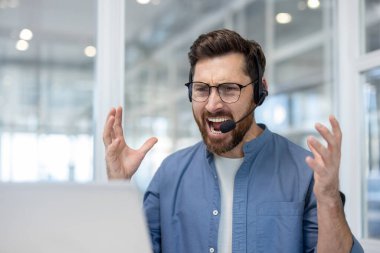 Ofis içi bilgisayar ve kulaklıkla otururken bağıran kızgın adam, ofis çalışanının video çağrısı..