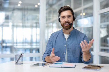 Webcam görüntüsü, kameraya bakan kulaklıklı adam, iş yerindeki meslektaşlarıyla uzaktan konuşuyor, danışman destek servisi asistanı..