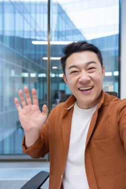 Video çağrısı, Asyalı bir adam telefon kamerasına bakıyor ve akıllı telefon uygulaması kullanarak iş arkadaşlarıyla konuşuyor. İş adamı ofis içi iş yerinde..