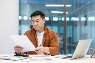 Evrak işlerinin arkasında ciddi bir adam, yatırım sözleşmelerini ve raporları kontrol eden olgun bir finansör. Not defteriyle evrak işleri arkasında başarılı Asyalı finansör.