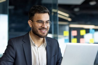 İşyerindeki başarılı iş adamı dizüstü bilgisayarla çalışıyor. Takım elbiseli adam çevrimiçi sunum okuyor ve hazırlıyor. Olgun patron dizüstü bilgisayara bakıyor.
