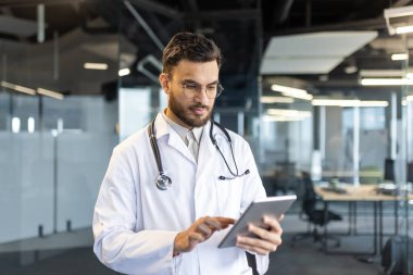 Klinikte tablet bilgisayarla çalışan ciddi bir erkek doktor. Doktor internetten hastalara danışmak için uygulama kullanıyor..