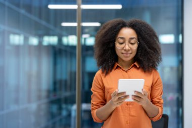 Pencerenin yanında tablet bilgisayarı olan ciddi bir kadın, iş kadını online uygulama kullanmayı düşünüyor. Ofis çalışanı ofis içinde, elektronik mali raporları okuyor..
