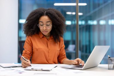 Ciddi bir muhasebeci, evraklarla, sözleşmelerle ve faturalarla uğraşan bir kadın. Ofis çalışanı dizüstü bilgisayarla mali raporlar dolduruyor..