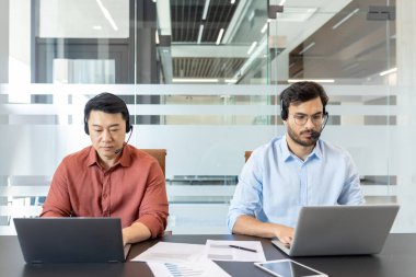 Ofis içinde laptopları ve kulaklıkları olan sıradan giysili iki meslektaş çalışıyor. Ofis çalışanları masada otururken müşterilere uzaktan danışıyorlar..