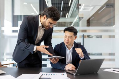İki iş adamı bir iş projesini tartışıyor, iş yerinde takım elbiseli bir adam iş yerinde. Bir çalışan tablet bilgisayarda bir çalışma programı gösterir.