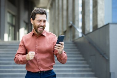 Ofis dışında başarılı bir adam zaferi ve zaferi kutluyor. İş adamı şehirde yürürken telefonla bildiri aldı. Ofis çalışanı gömlekli, elinde akıllı telefon var..
