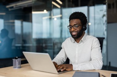 Ofis içinde çalışan kulaklık ve dizüstü bilgisayarı olan genç bir adam. Uzaktan kumandalı hastalara gülümseyen destek çalışanı. Çevrimiçi yardım hattı.