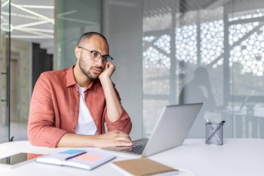 Bilgisayarın başında oturmaktan sıkılmış bir adam, iş yerinin içinde ofis çalışanı. Çok çalışılmış.