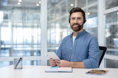 Video çağrısı, kulaklık ve tablet bilgisayarlı bir adam kameraya bakıyor. İş yerindeki destek çalışanı müşterilere uzaktan danışmanlık ve yardım yapıyor. Ofis çalışanı..
