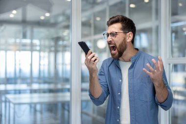 İş yerindeki kızgın adam telefon ahizesine bağırıyor. İş adamı, ofisin ortasında rahat olmayan, sinirli bir patron..