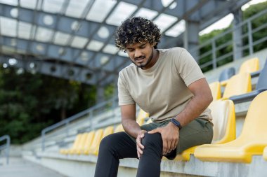 Bir adam aktif fiziksel egzersiz ve spor yaparken bacağını yaraladı. Bir sporcu, otururken diz kaslarına masaj yapıyor..