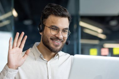Ofis içinde kulaklığı ve bilgisayarı olan bir adam. Çevrimiçi müşteri destek çalışanı görüntülü arama kullanarak konuşuyor. İş adamı iş arkadaşlarıyla iş toplantısını kapatıyor.