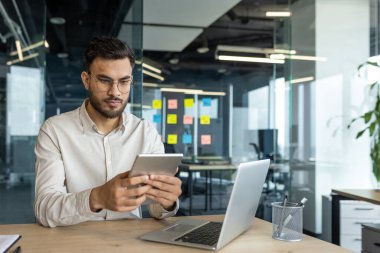 Ofisin içinde tablet bilgisayarla çalışan ciddi bir iş adamı. İş yerinde çalışan iş adamı, dizüstü bilgisayar kullanıyor, masada oturuyor, finansal uygulama kullanıyor..