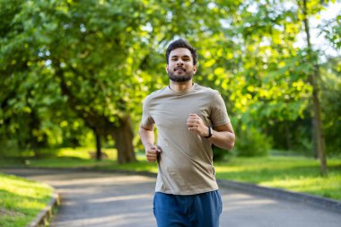 Spor giyimli Hintli genç adam spor yapıyor ve parkta koşuyor..