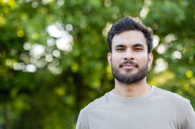 Park yerinde duran kendine güvenen sakallı bir adamın portresi. Arka plandaki yeşil ağaçlar açık hava ortamını vurguluyor. Doğal ışıklandırma canlı ve taze bir his sunar..