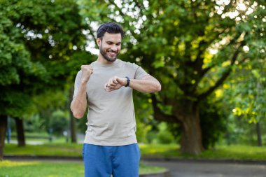 Parkta spor yapmaktan hoşlanan bir adam, akıllı adam hareketlerini kontrol ediyor. Sıradan sporlar yapmak, motive olmak ve başarılı olmak. Parlak yeşil ortam odaklanmayı ve dışarıda çalışmayı arttırır.
