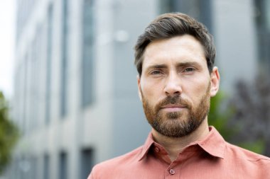 Ofis binasının dışında kendine güvenen ciddi bir adamın portresi. Kırmızı gömlekli iş adamı kameraya bakıyor. Şirket çalışanı düşünüyor ve odaklanıyor.