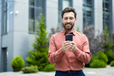 Ofis binasının dışında elinde telefonla dolaşan başarılı bir adam var. İş adamı akıllı telefonunda bir uygulama kullanıyor, mesajlar yazıyor, sosyal medyada geziniyor, gülümsüyor..