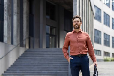 Bir ofis çalışanı elinde evrak çantasıyla bir ofis binasının önünde yürüyor. Sıradan giyinmiş bir işadamı mutlu bir şekilde gülümser..