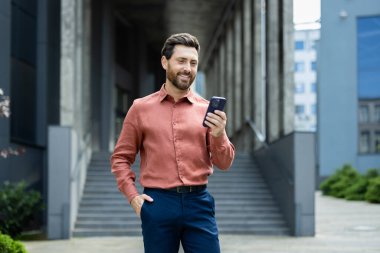 Ofis binasının önünde dururken akıllı telefon kullanan kendine güvenen iş adamı..