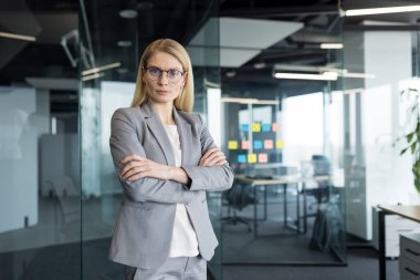 Ofisteki kendine güvenen iş kadını patronunun portresi. İş elbiseli kadın, elleri bağlı kameraya özgüvenli ve zarifçe bakıyor..
