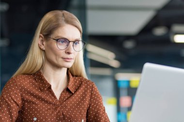 İş yerinde laptopla çalışan olgun bir kadın masasında otururken bilgisayar ekranına bakan iş kadını kendinden emin ve konsantre..