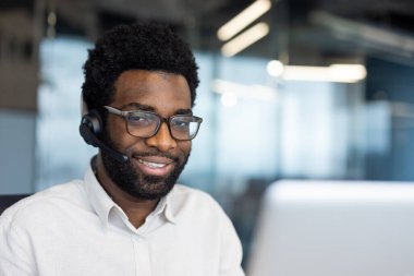 Bir destek işçisinin portresi, kulaklık takmış gülümseyen ve kameraya bakan bir adam. Ofisin içinde dizüstü bilgisayarı olan bir şirket çalışanı.
