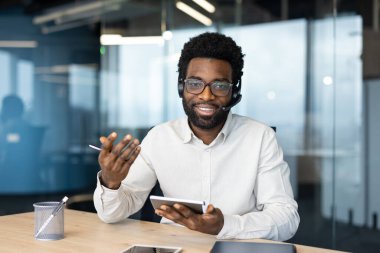 Webcam görüntüsü, kulaklıklı bir adam kameraya bakıyor, iş arkadaşları ve ortaklarıyla uzaktan video görüşmesi yapıyor. Gülümseyen ve arkadaş canlısı çevrimiçi müşteri destek çalışanı.