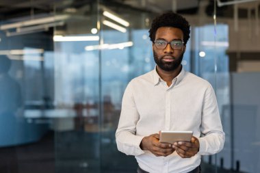 Ciddi odaklanmış bir adam kameraya bakıyor. İş yerindeki ofis binasının içinde elinde tablet bilgisayarla duran bir iş adamı. Akşamları çalışıyorum..
