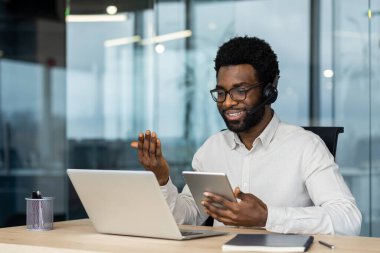 İş yerinde elinde telefon ve tablet bilgisayarla destek servisi çalışanı. Adam müşterilere uzaktan video bağlantısı kuruyor. İş toplantısı konferansı..