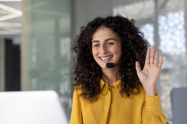Kulaklık takmış bir kadın, ofis çalışanı iş arkadaşlarını ve arabulucuları selamlarken el sallıyor. Çevrimiçi iş toplantısındaki iş kadını, uzak konferans. Destek servisi çalışanı.