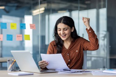 Başarılı bir kadın iş yerinde başarı kazanmayı kutluyor. İş kadını raporunu tutuyor, elinde belgelerle, zaferle el ele tutuşuyor..