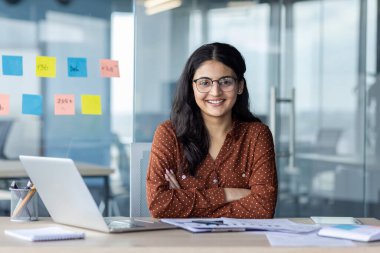 İş yerindeki başarılı, neşeli kadın finansörün portresi. Çapraz kollu iş kadını gülümseyen ve kameraya bakan, evraklar ve raporlarla masada oturan..