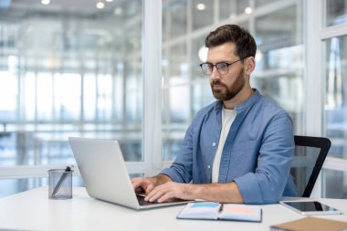 İş yerinde bilgisayarla çalışan, klavyede yazan ciddi düşünen bir adam..