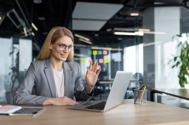 Çevrimiçi video konferansı, iş yerindeki başarılı iş kadını patronu video görüşmesi için laptop kullanıyor. İş elbiseli bir kadın iş arkadaşlarını ve ortaklarını selamlıyor. İş toplantısı.