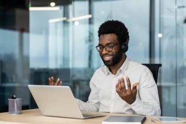 Kulaklıklı neşeli gülen adam meslektaşları ve ortaklarıyla uzaktan konuşuyor. İş yerinde destek işçisi, müşterilere uzaktan yardım eden danışman..