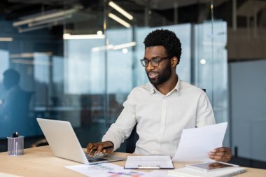Başarılı bir iş adamı ofis içinde evrak işleriyle uğraşıyor, raporlar hazırlıyor, belgeler ve kağıtlarla uğraşıyor. Şirket çalışanı muhasebecisi, elinde mutlu bir şekilde gülümseyen bir kontrat tutuyor..