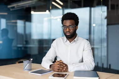 Adam, modern ofis ortamında bir video görüşmesi sırasında dikkatle dinliyor, sanal toplantı sırasında nişan ve odaklanma sergiliyor
