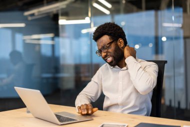 Boyun ağrısından muzdarip yorgun ve çok çalışan bir adam. İş yerinde çalışan bir iş adamı. Elleriyle boyun kaslarına masaj yapıyor. Ofiste dizüstü bilgisayarla uzun ve monoton bir şekilde oturuyor..