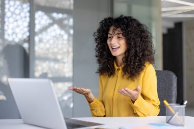 Modern bir ofis ortamında, canlı bir video görüşmesi sırasında bir kadın gülümsüyor.