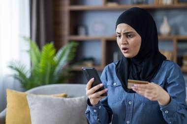 Ortadoğulu tesettürlü bir kadın kredi kartı ve telefonuyla internet üzerinden ödeme yapmakta zorlanıyor..