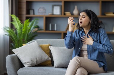 Oturma odasında kanepede otururken astım krizi geçiren ve nefes darlığı çeken genç bir kadın..