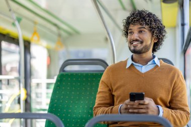 Telefonu elinde olan mutlu adam toplu taşıma araçlarında geziyor, yolcu gülümsüyor ve pencereden dışarı bakıyor, sosyal medyada gezinmek için akıllı telefon uygulaması kullanıyor..