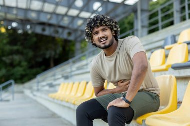 Mide ağrısından muzdarip bir adam, sporcu aktif fitness sonrası dinleniyor ve koşuyor, el ele tutuşuyor. Parkta yürüyorum..