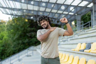 Sporcu aktif fiziksel egzersizler ve fitness yaparken yaralandı. Adam dışarıda parkta durmuş, omuz ve sırt kaslarına masaj yapıyor.