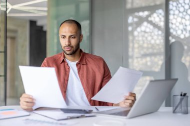 Ciddi odaklı finans işadamı evrak işleriyle uğraşıyor, belgeleri kontrol ediyor, raporları hazırlıyor. Ofis çalışanı bilgisayarla çalışmayı düşünüyor..