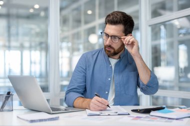 Ofisin içinde bilgisayarla çalışan ciddi bir finansör muhasebecisi. Evrak işleri yapan, vergi formlarını dolduran bir adam. İş adamı rapor hazırlıyor, ofis içi belge imzalıyor..